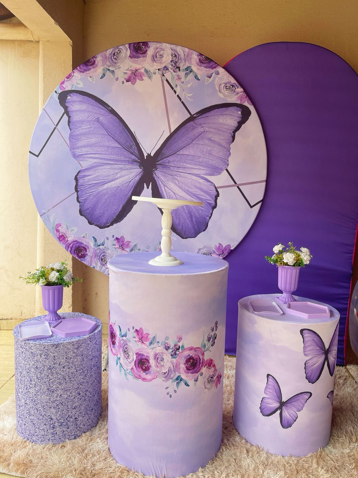 Decoração de festa com painel de borboleta lilás e flores, cilindros em tons de lilás