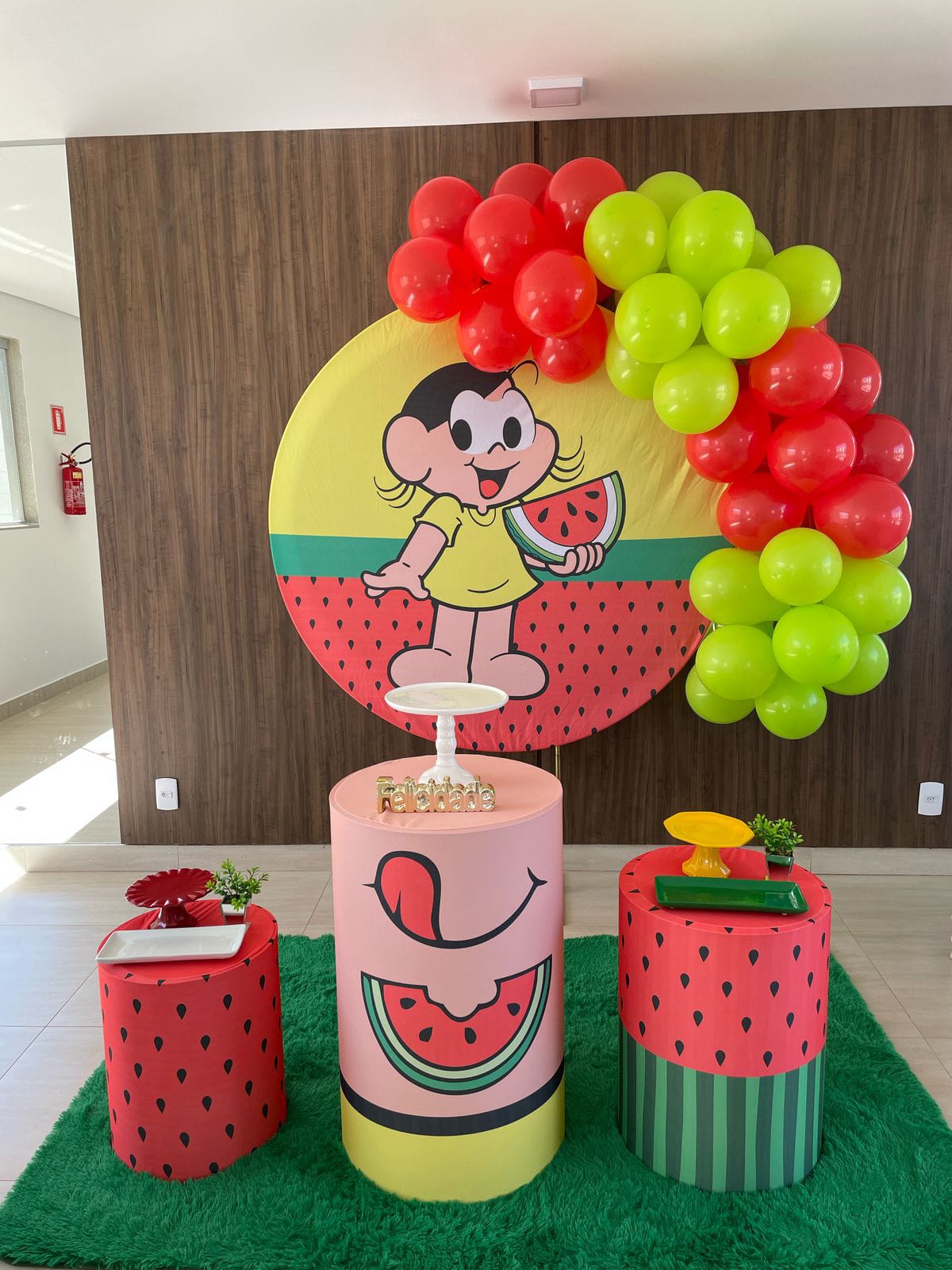 Decoração de festa infantil com painel de personagem e melancia, balões vermelhos e verdes