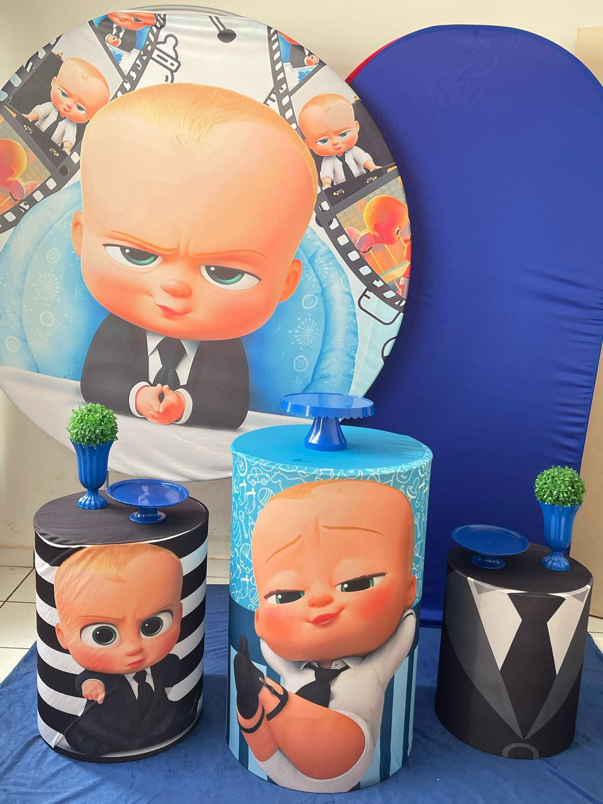 Decoração de festa com painel de O Poderoso Chefinho e cilindros azuis e listrados